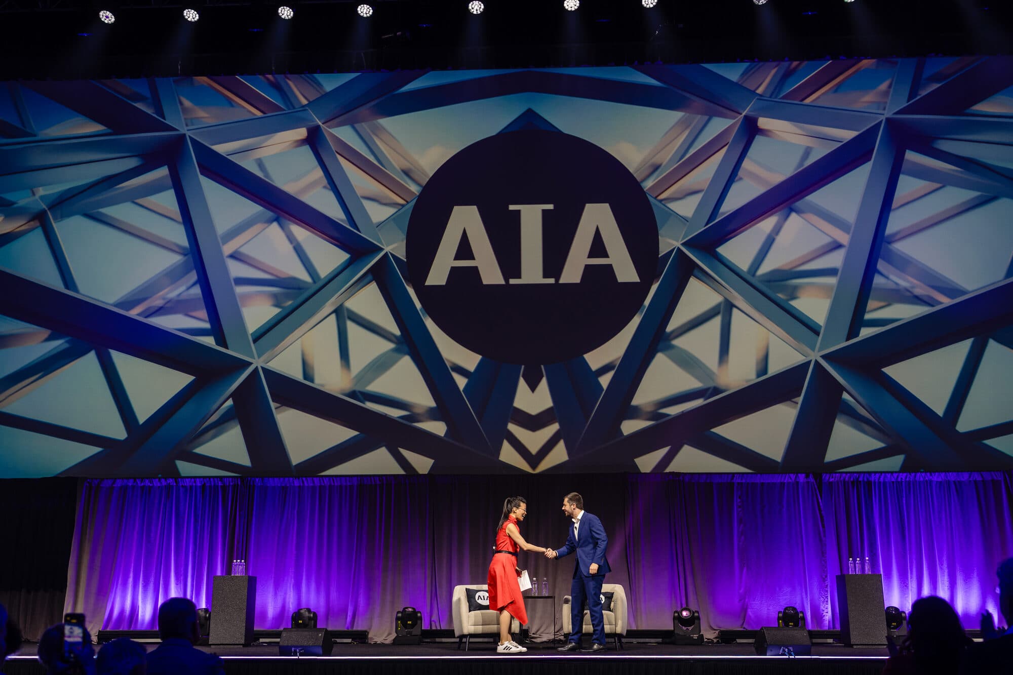 Evelyn Lee shaking hands with Pete Buttigieg on stage at the AIA25 Conference keynote, June 2025.